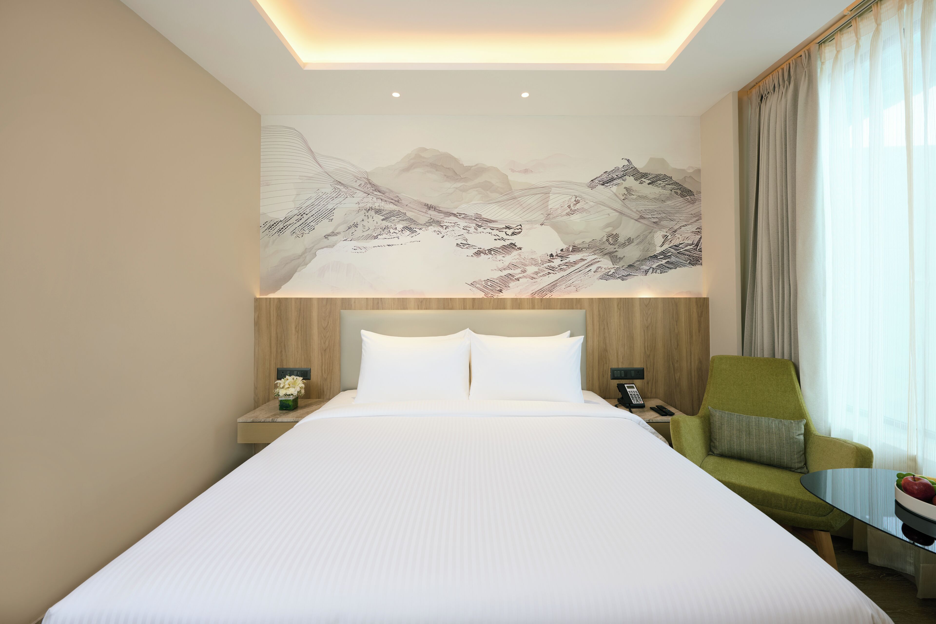 A hotel room with a large bed, a nightstand with a phone, a green armchair, and a wall-mounted artwork.