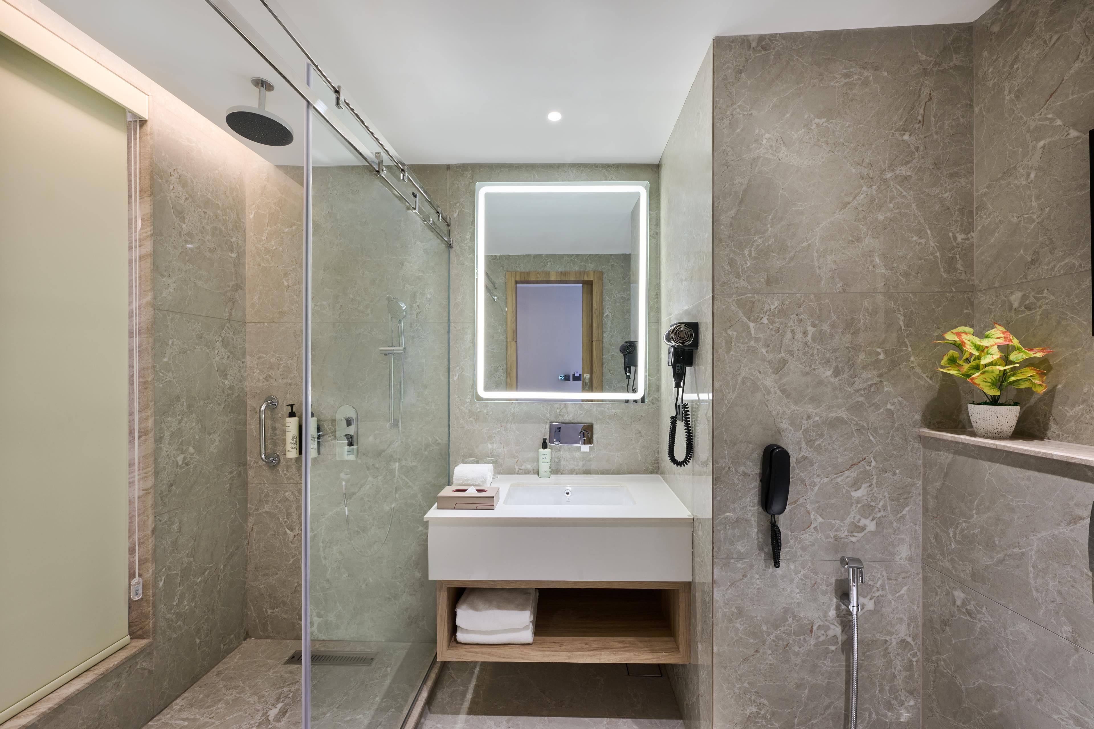 Un baño moderno con ducha envuelta en vidrio, un lavamanos blanco e iluminación integrada en el espejo.