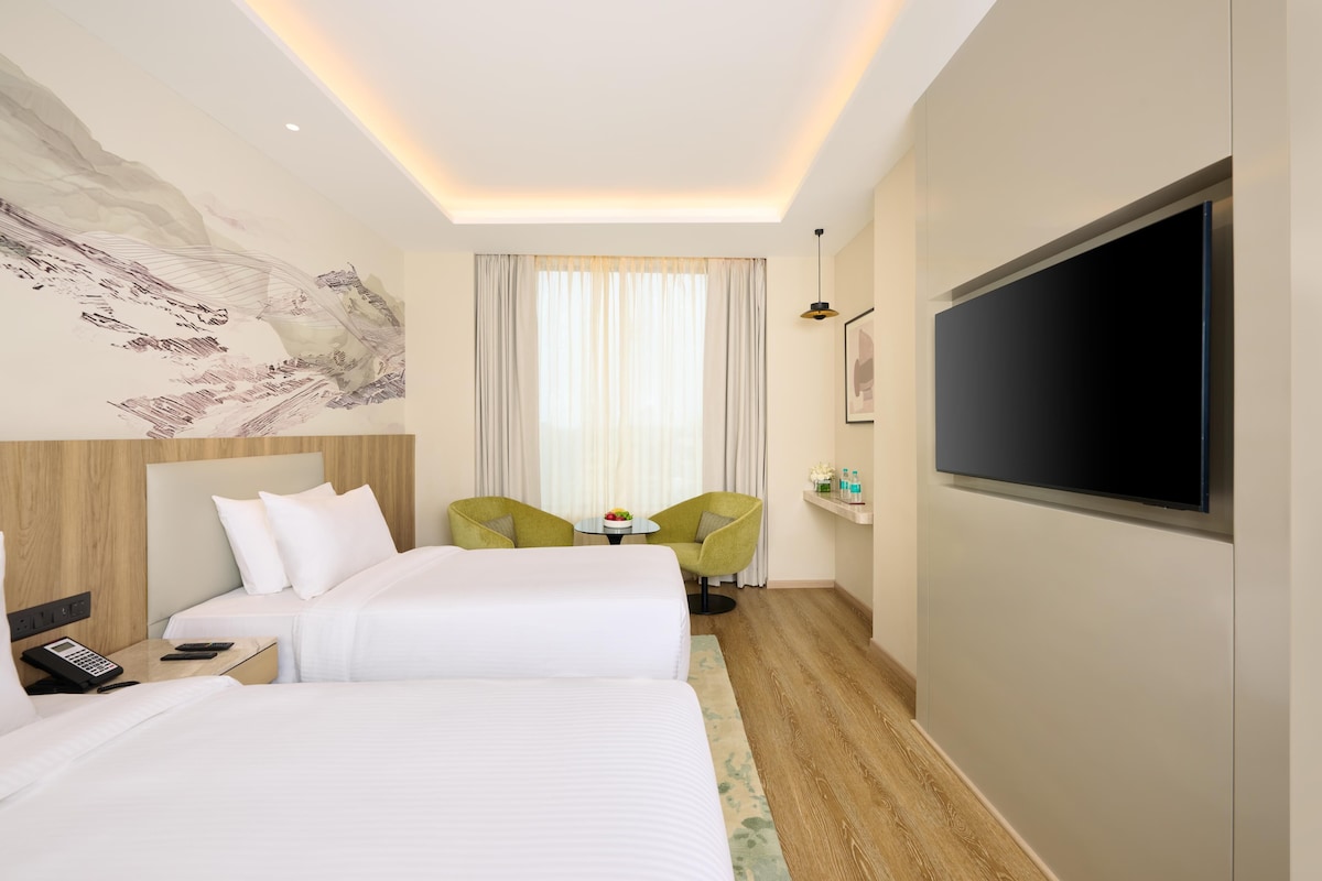 A hotel room with two beds, a TV, a desk with a phone, a chair, and a wall-mounted TV.
