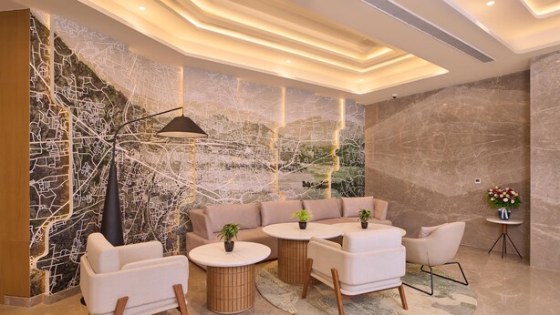 A modern lounge area with a sectional sofa, round tables, and a decorative wall with a map design. - Riviera Sarovar Portico Pathankot (Pathankot)