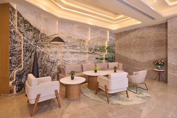 A modern lounge area with a sectional sofa, round tables, and a decorative wall with a map design. - Riviera Sarovar Portico Pathankot (Pathankot)