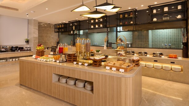 Un buffet de petit-déjeuner proposant une variété d’aliments et de boissons, un coin café et un espace cuisine en arrière-plan.