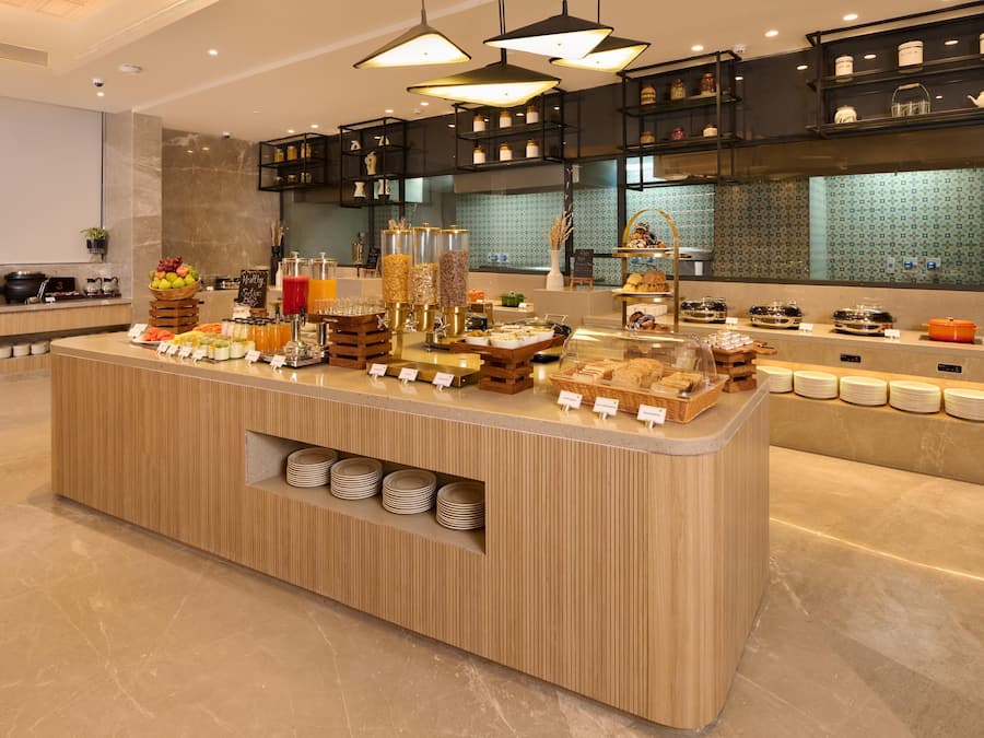 A breakfast buffet with various food items and beverages, a coffee station, and a kitchen area in the background.