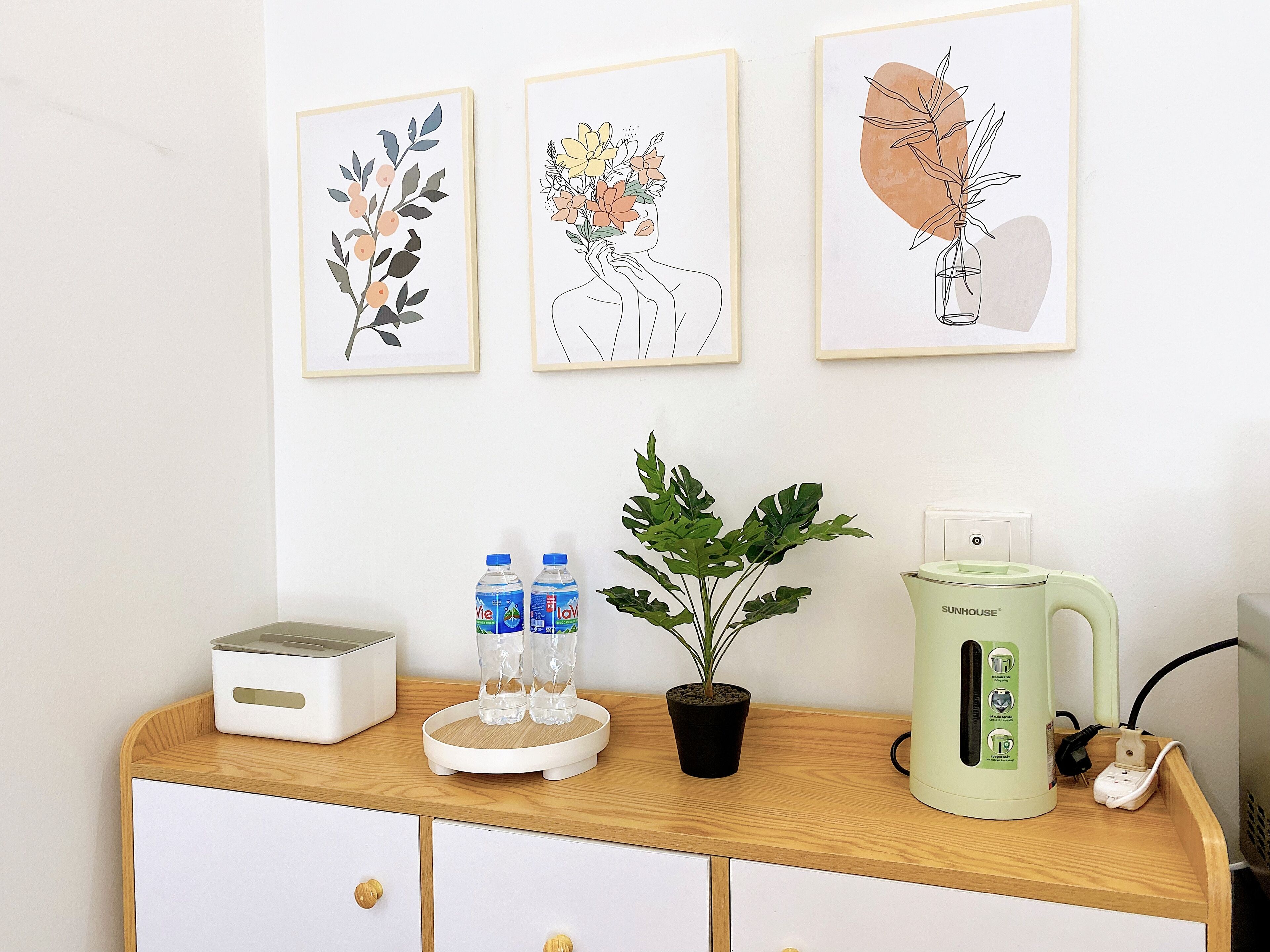 A wooden cabinet with a white appliance, two water bottles, a potted plant, and a green kettle.