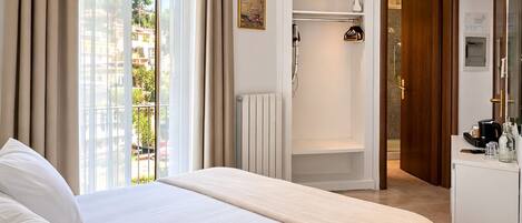 A hotel room with a bed, a shower, a TV, and a view of buildings outside.
