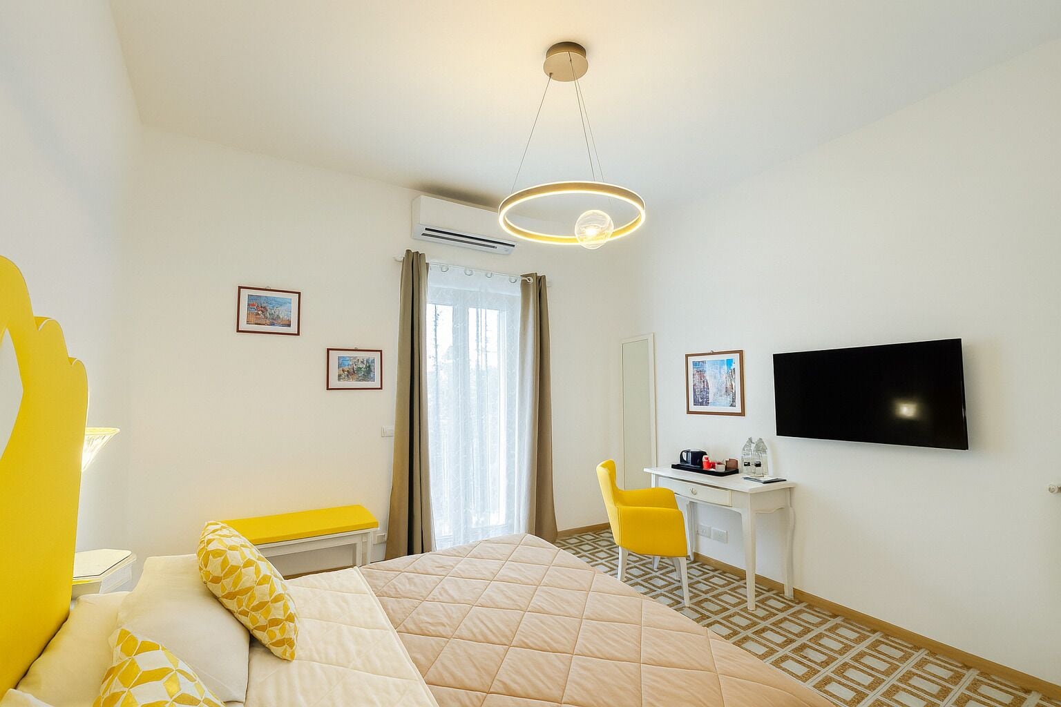 Habitació d'hotel amb llit, escriptori, cadira, televisió i finestra amb cortines.