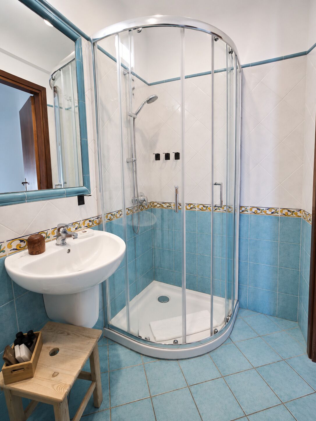 Une salle de bain avec une douche à parois de verre, un lavabo et un tabouret en bois.