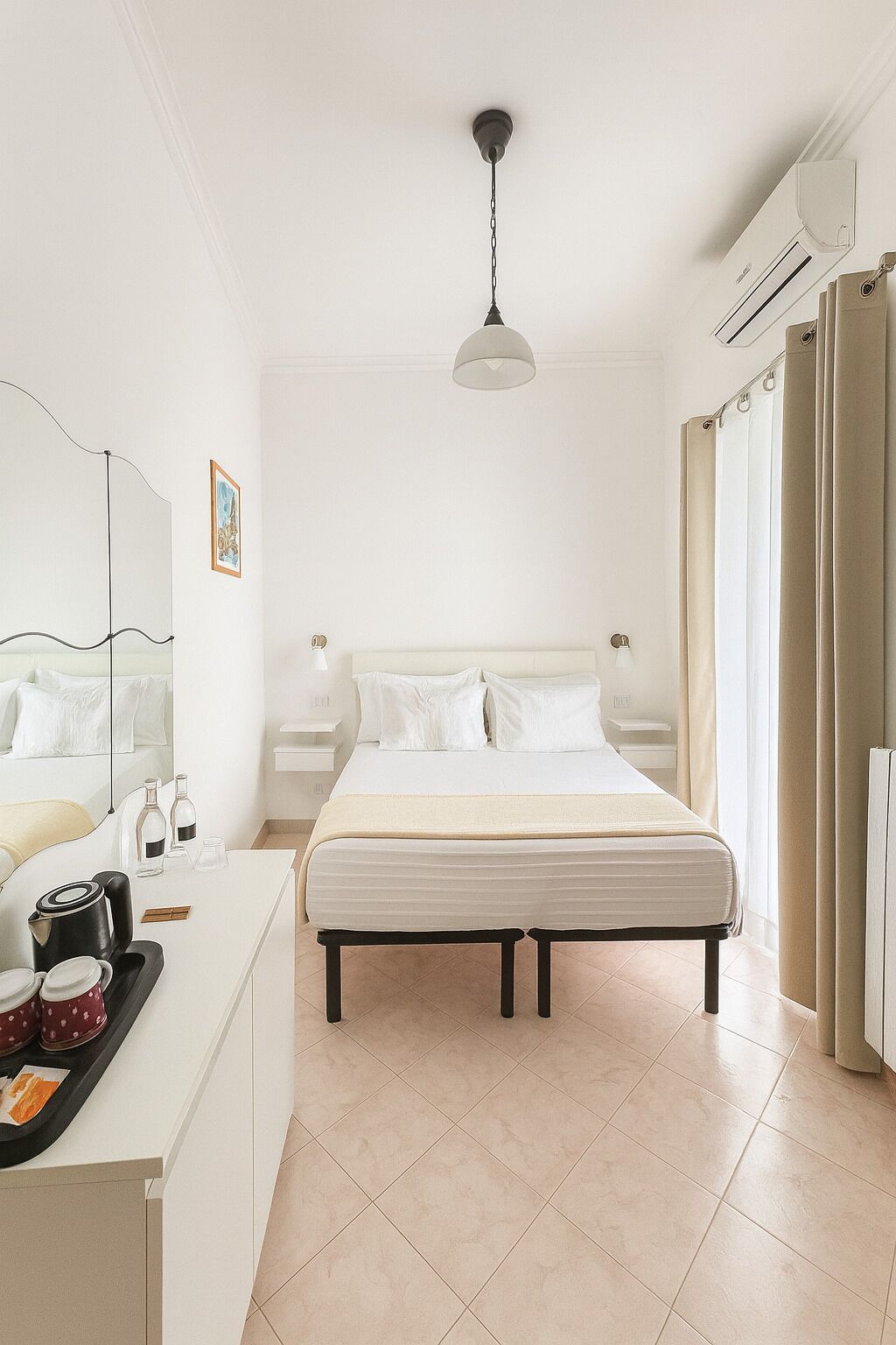 A hotel room with a bed, bedside tables, a desk with a coffee maker, and a hanging light fixture.