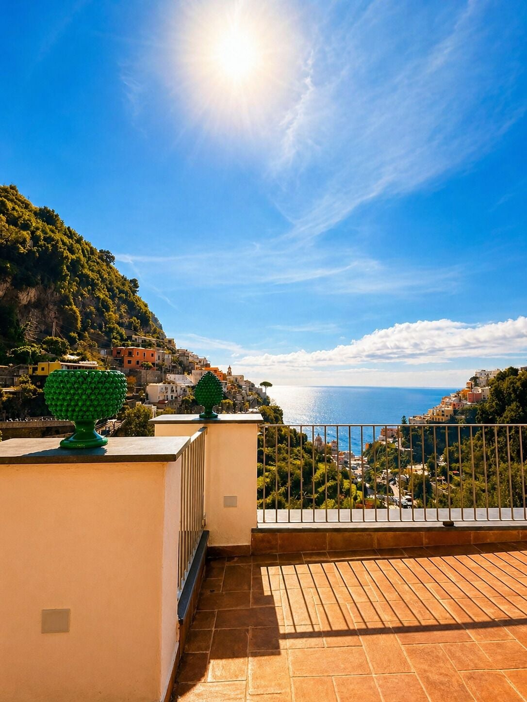 A terrace with a view of a coastal town, a railing, and a tiled floor.