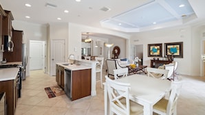 Una cocina amplia con una isla central, muebles blancos y una zona de comedor con una mesa grande y sillas.