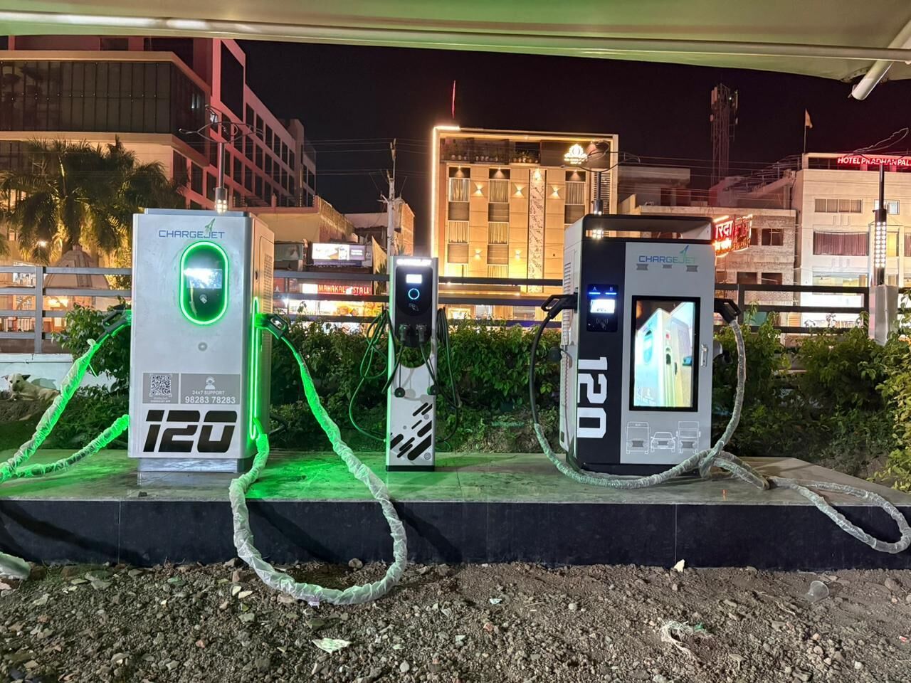 Drei Ladestationen für Elektroautos mit digitaler Anzeige, verbunden durch Kabel, unter einer Überfahrt bei Nacht.