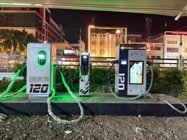 Tre stazioni di ricarica per veicoli elettrici con display digitale, collegate da cavi, sotto un viadotto di notte.
