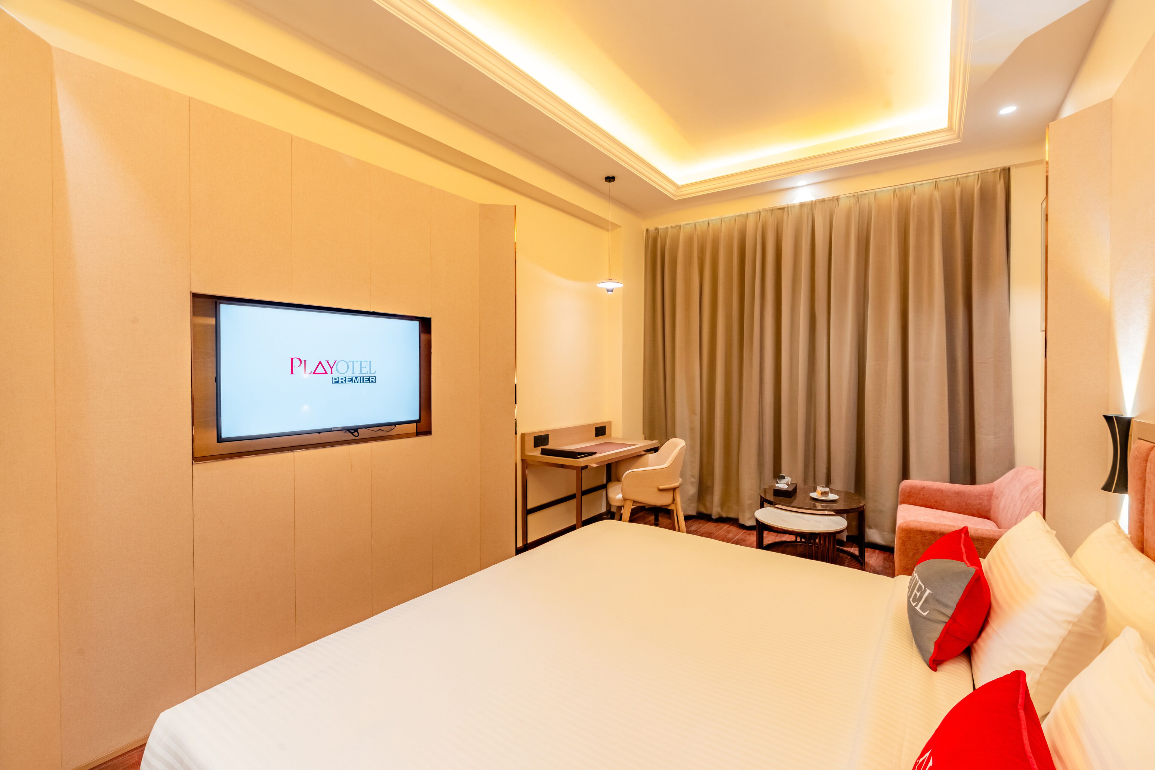 A hotel room with a bed, a desk, a chair, a TV, and a window with curtains.