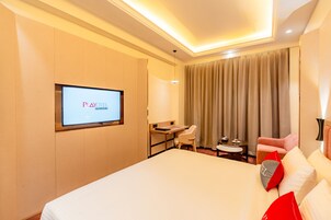 A hotel room with a bed, a desk, a chair, a TV, and a window with curtains.