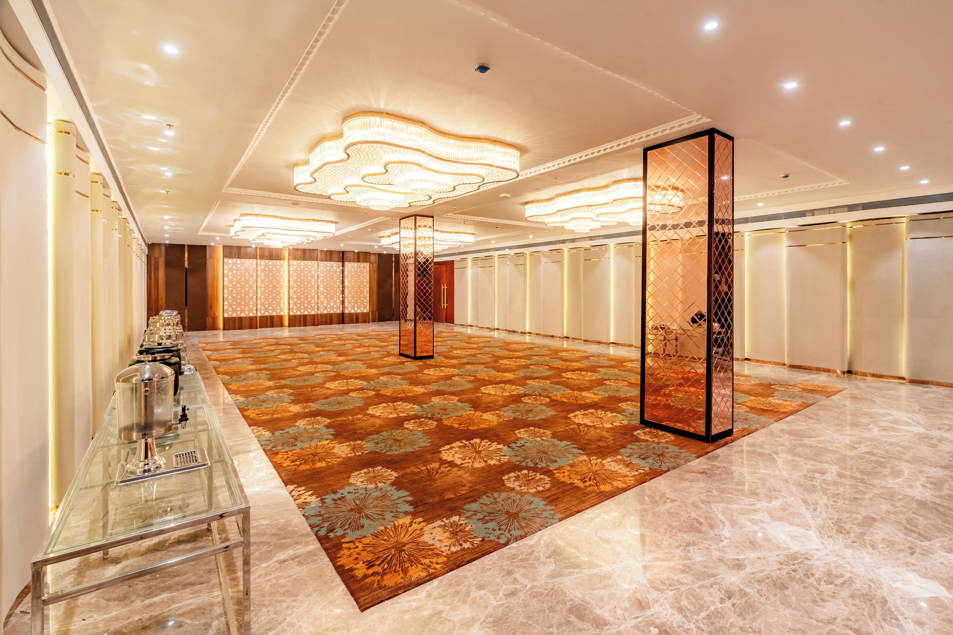 A spacious hotel lobby with a long reception desk, a patterned carpet, and a modern chandelier.