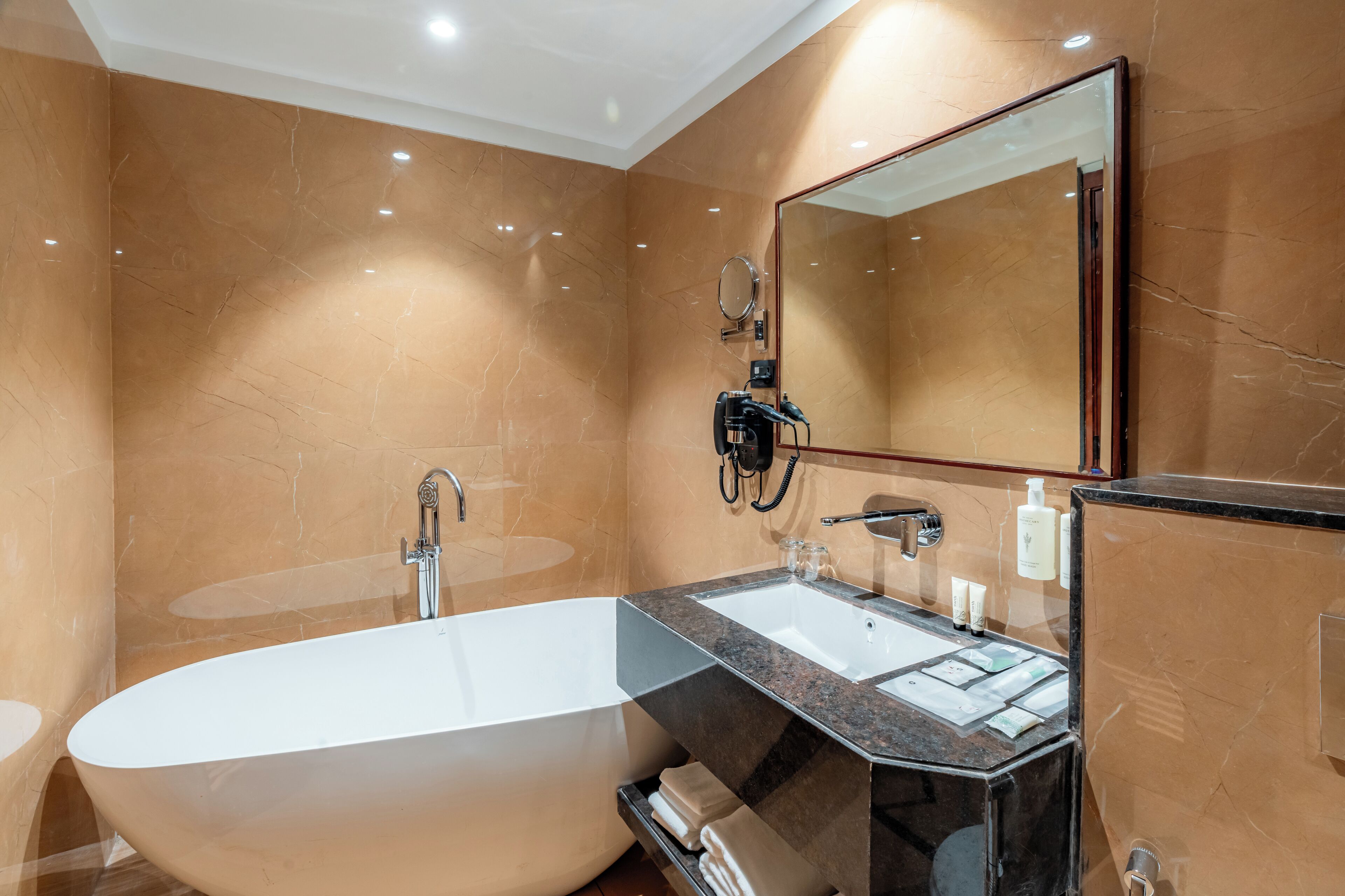 Een moderne badkamer met een vrijstaand bad, een wastafel met spiegel en marmeren wanden.