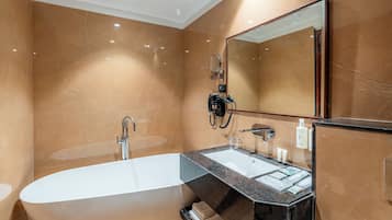 A modern bathroom with a freestanding bathtub, a vanity with a mirror, and marble walls.