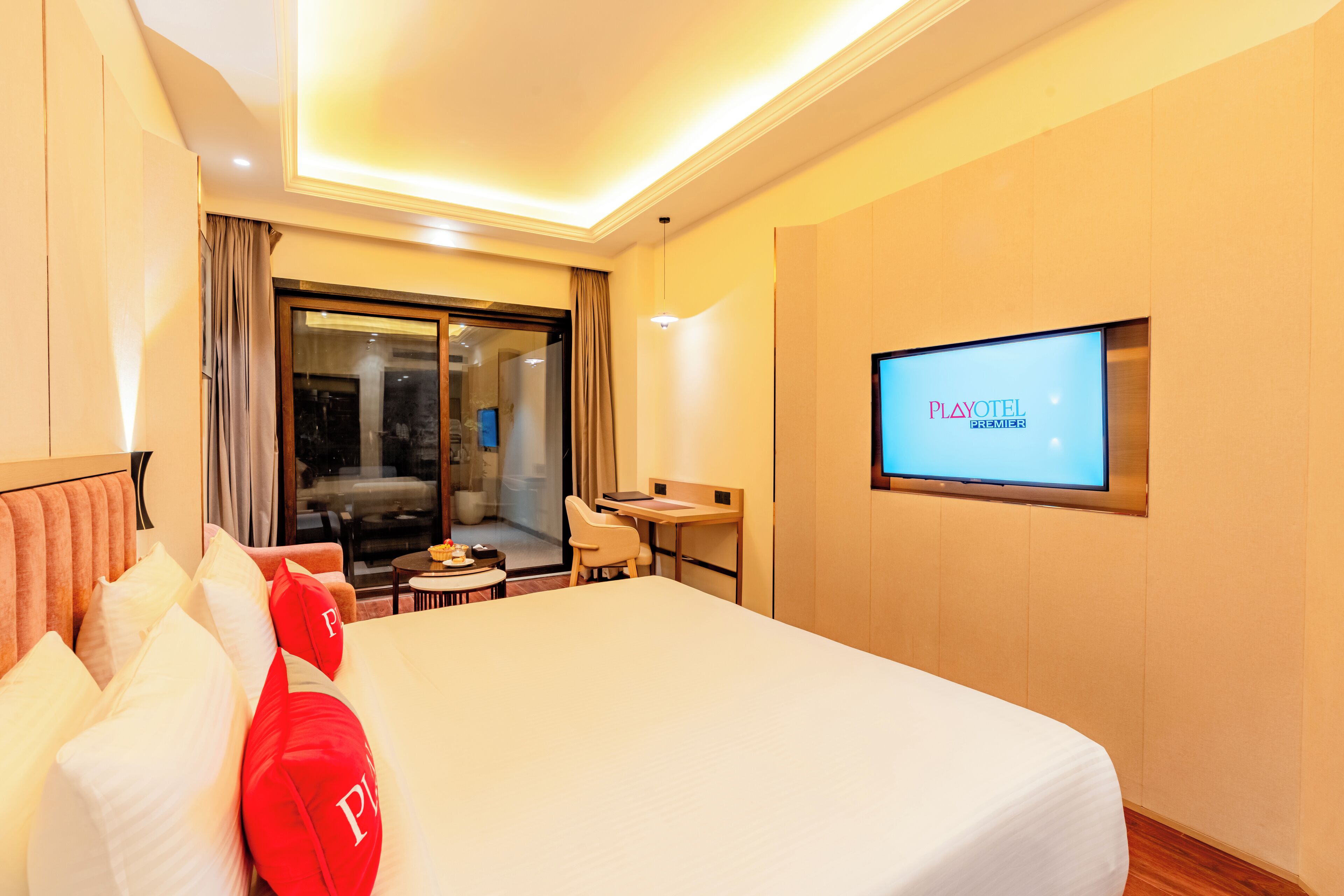 A hotel room with a large bed, a desk, a chair, a TV on the wall, and a sliding door to the balcony.