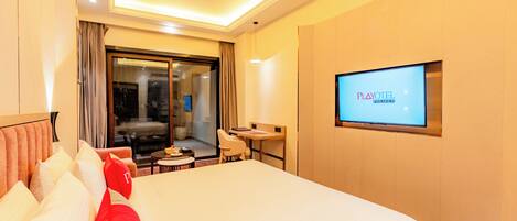 A hotel room with a large bed, a desk, a chair, a TV on the wall, and a sliding door to the balcony.