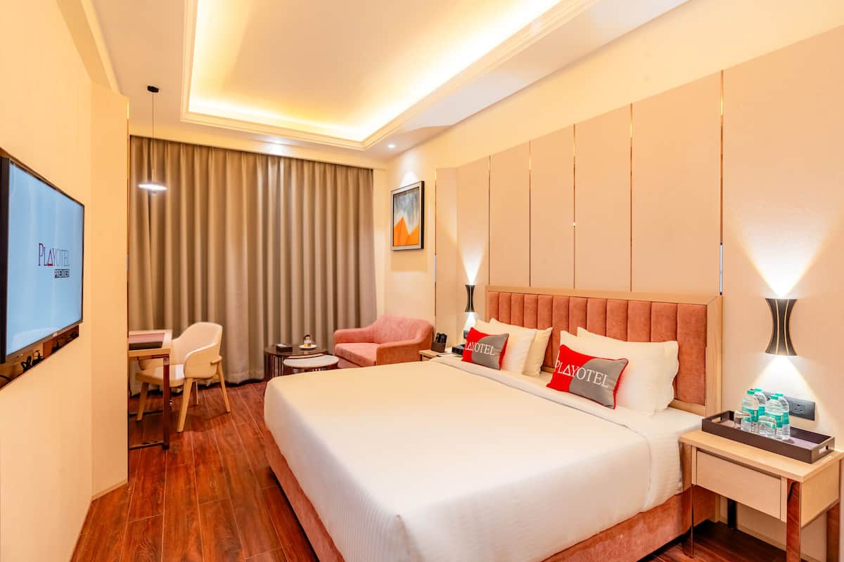 Une chambre d’hôtel avec un grand lit, un bureau avec une chaise, une télévision et une table de chevet sur laquelle se trouve un plateau avec des bouteilles d’eau.