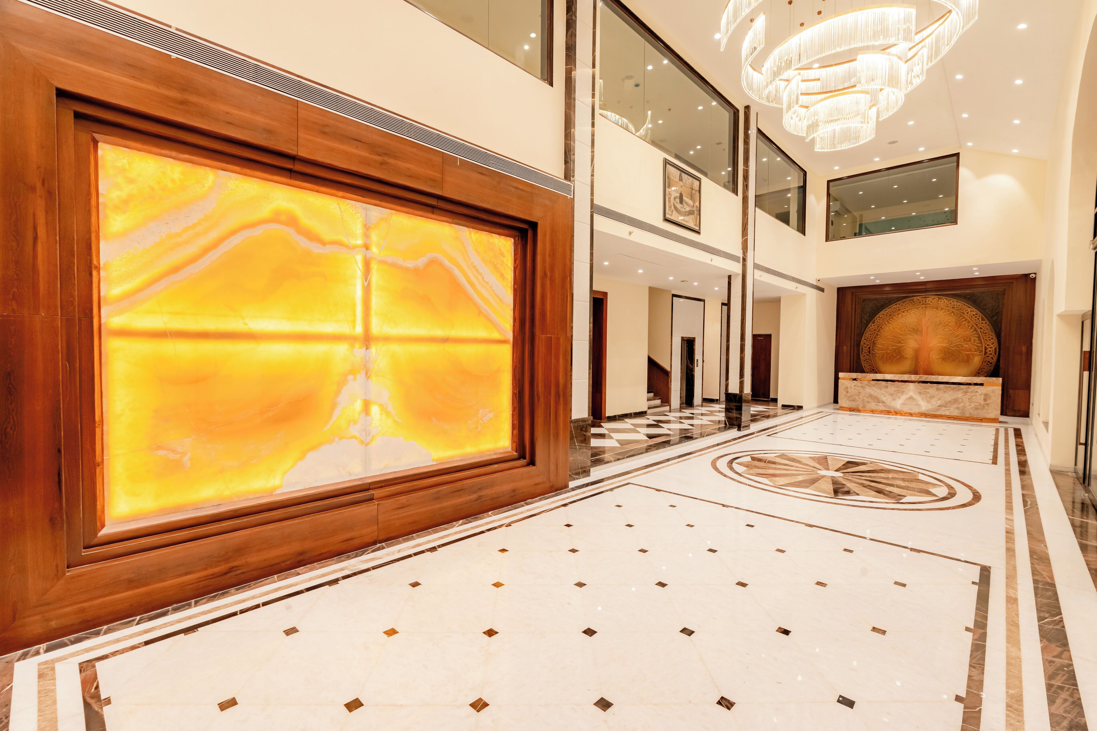Un hall d’entrée spacieux, orné d’un grand mur de marbre, d’un lustre imposant et d’un motif de carreaux sur le sol.