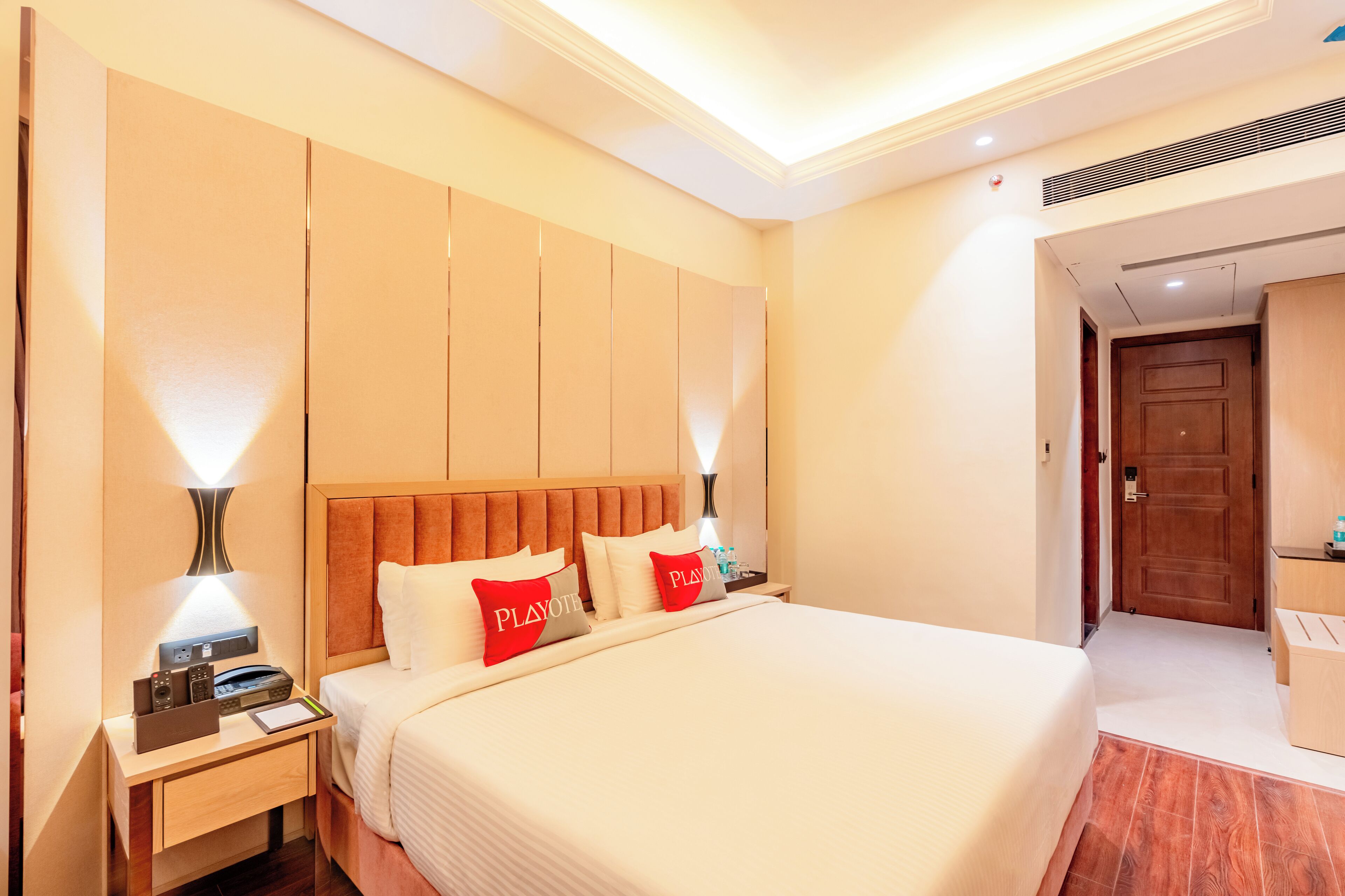 A hotel room with a large bed, bedside tables, a wooden headboard, and a door leading to another room.