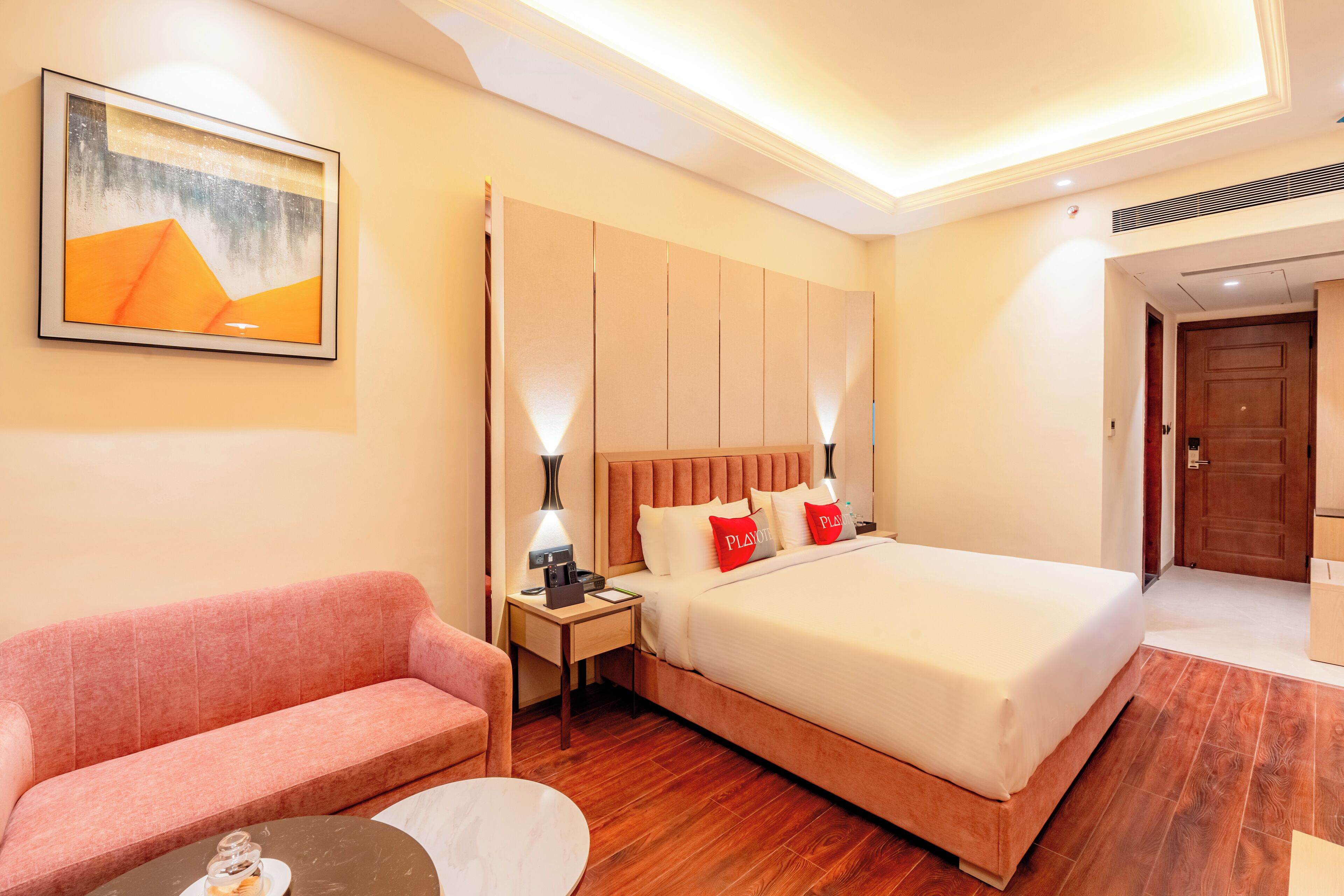 A hotel room with a bed, a sofa, a small table, and a painting on the wall.