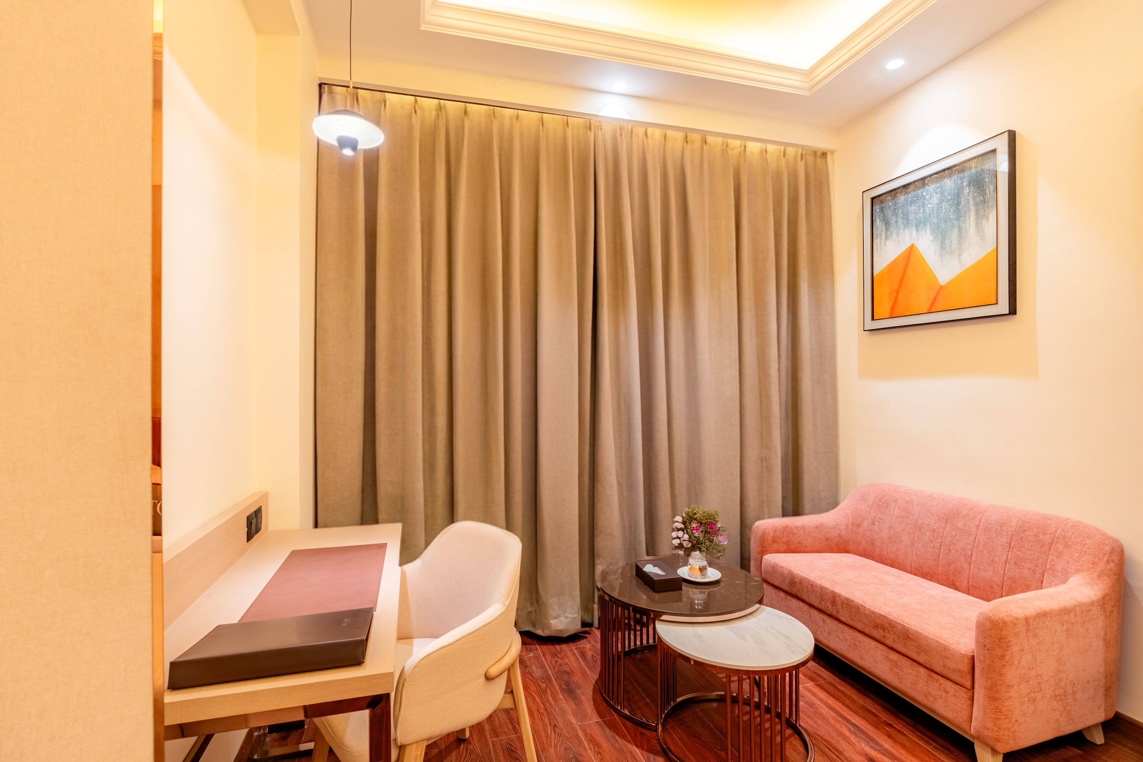 A hotel room with a desk, chair, pink sofa, and a painting on the wall.