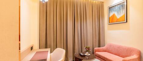 A hotel room with a desk, chair, pink sofa, and a painting on the wall.
