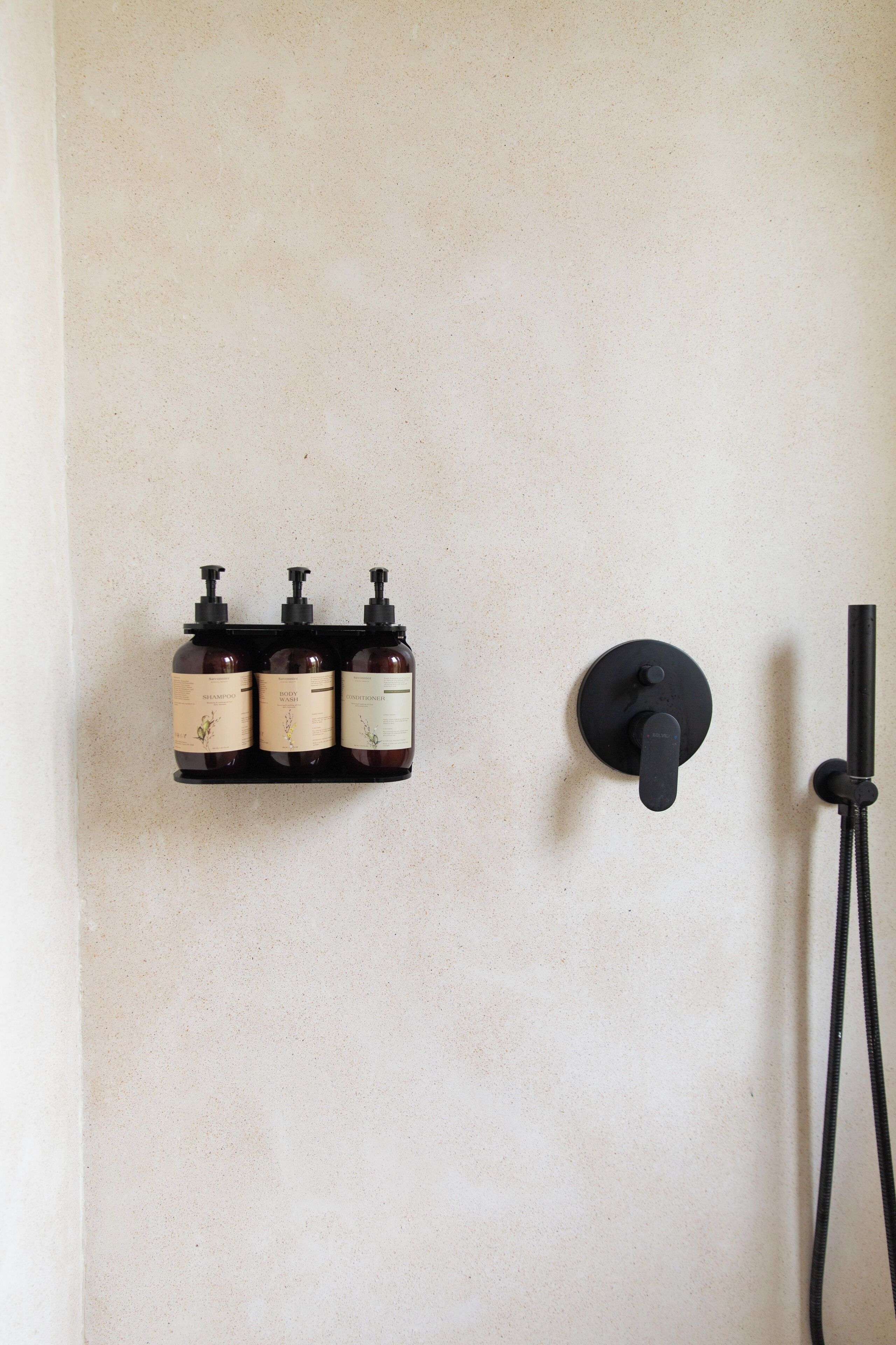 A bathroom with a wall-mounted soap dispenser set and a handheld showerhead.