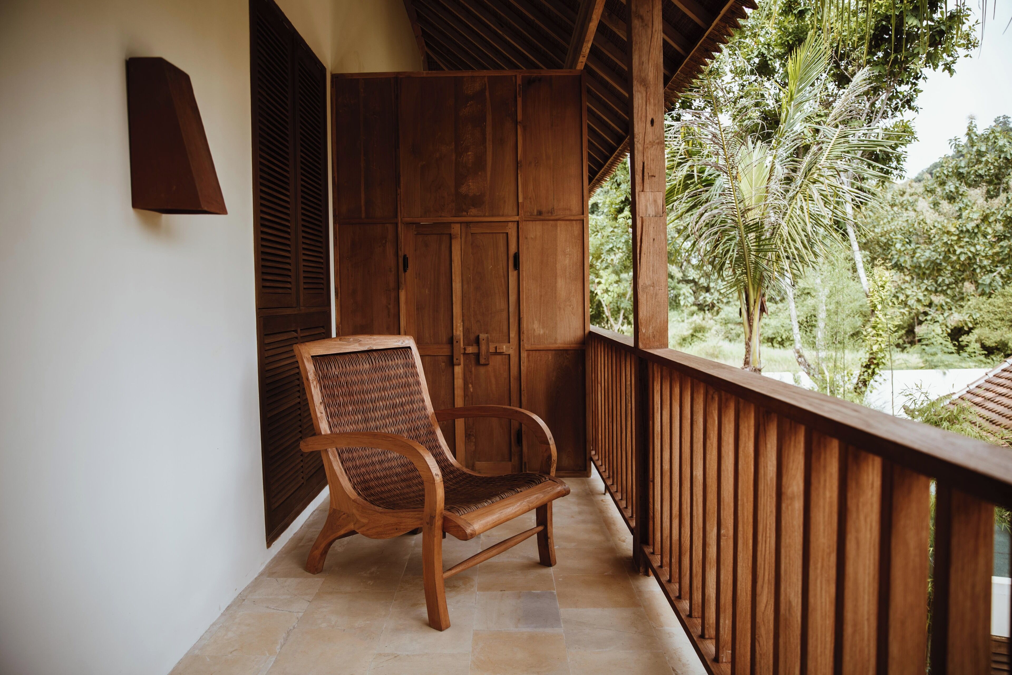 Una sedia di legno su un balcone con vista su del verde e una porta in legno.