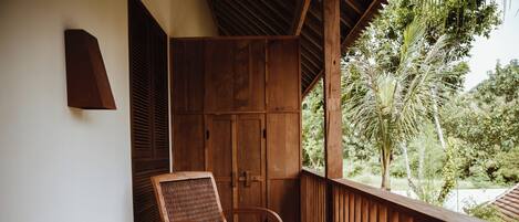 Una sedia di legno su un balcone con vista su del verde e una porta in legno.