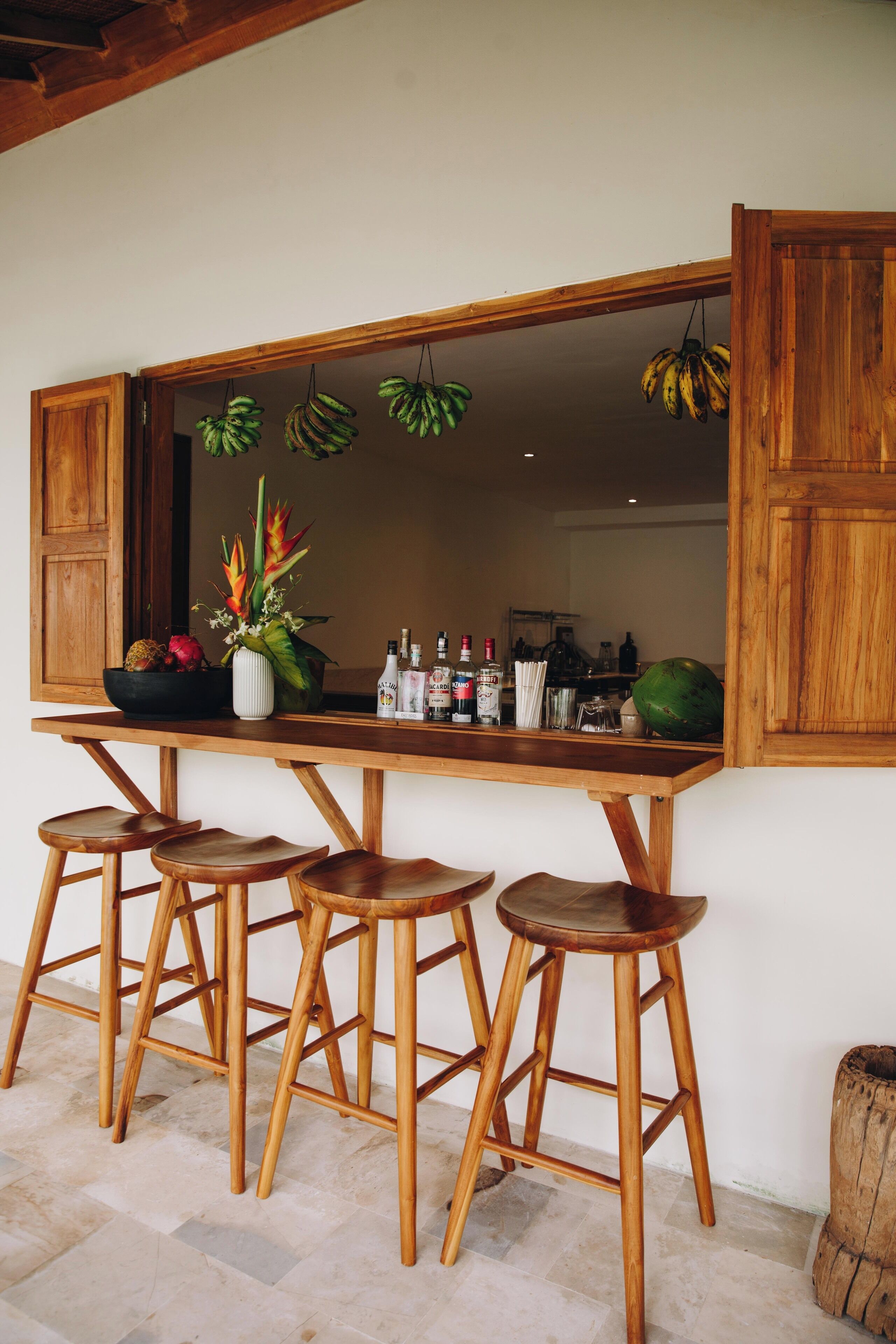 Una barra de madera con taburetes, un espejo grande y plátanos colgando.
