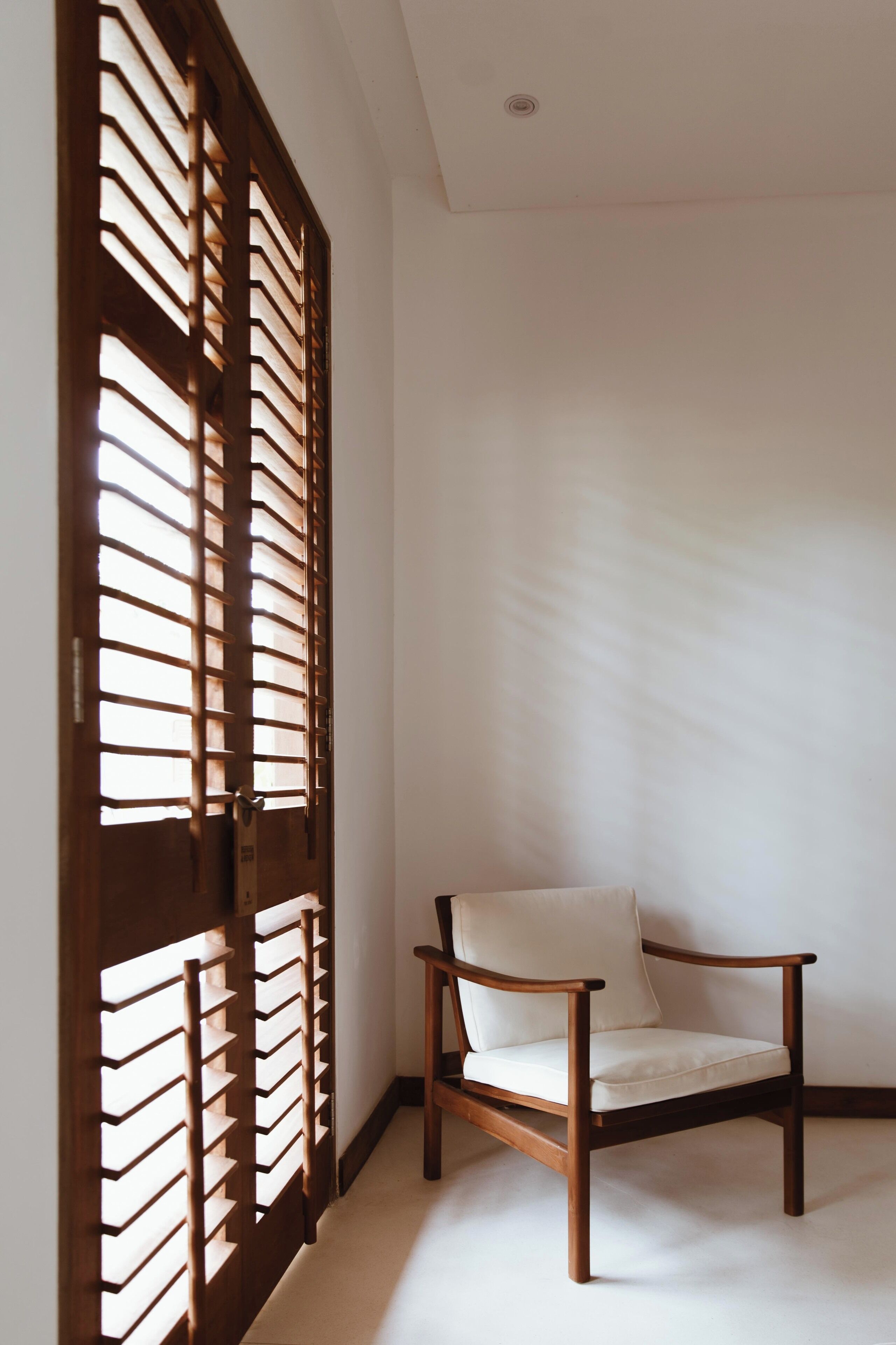 Une pièce avec une chaise en bois, une porte en bois dotée d’une fenêtre et un mur blanc uni.