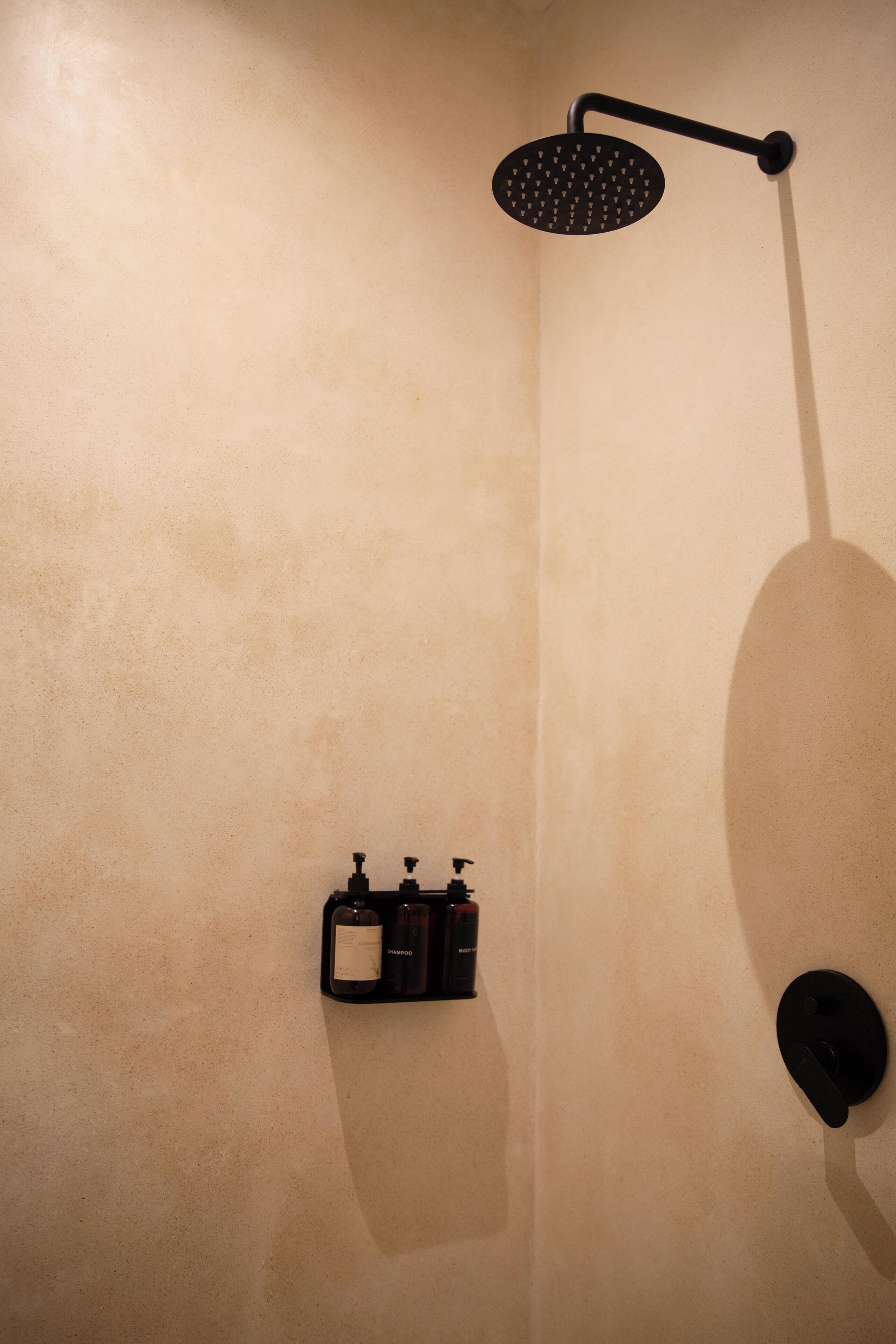 A bathroom with a shower, a soap dispenser, and a bottle of shampoo.