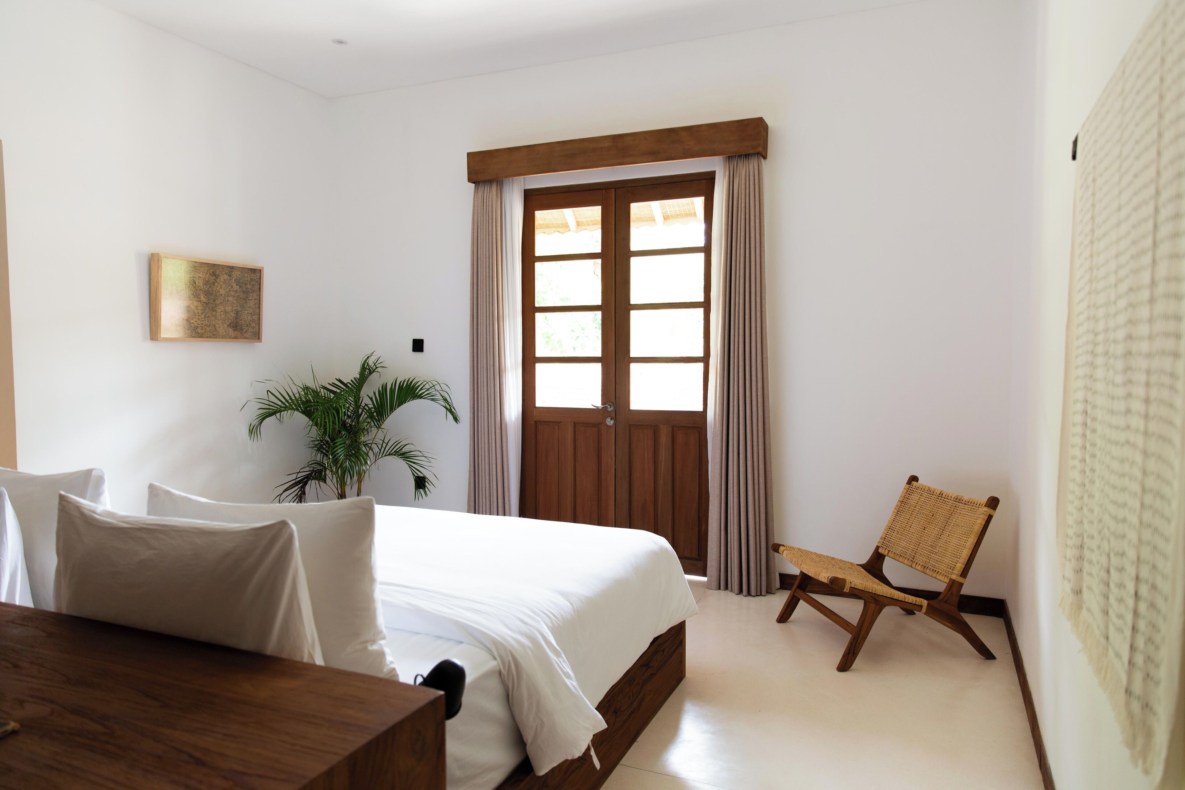 A bedroom with a bed, a wooden chair, a potted plant, and a door with curtains.