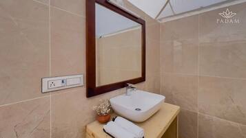 A bathroom with a large mirror, a white sink, a wooden vanity, and a small potted plant.