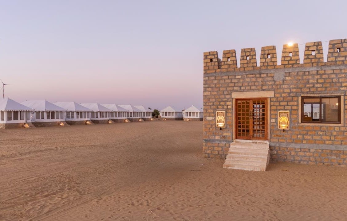 A desert landscape with white tents and a stone building with a wooden door and windows.