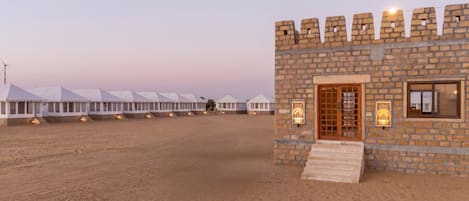 A desert landscape with white tents and a stone building with a wooden door and windows.