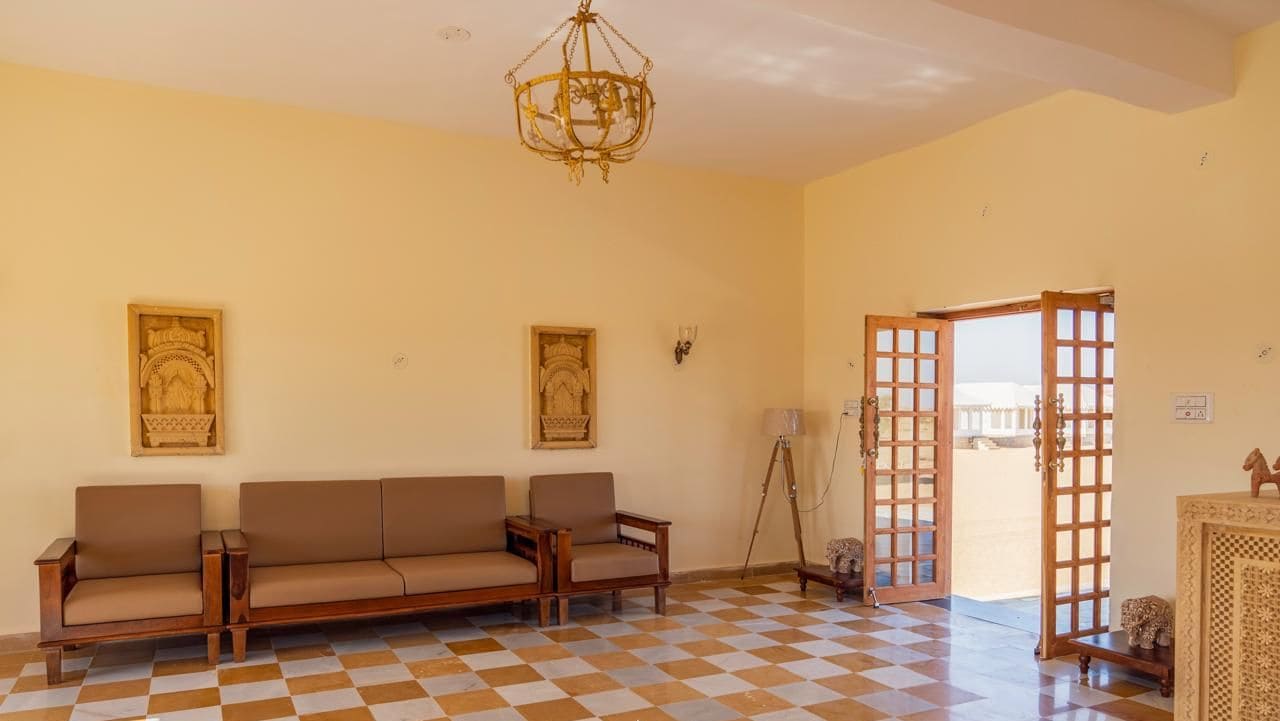 Una habitación con piso a cuadros, un conjunto de sofás, una araña y dos puertas que dan al exterior.