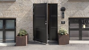 Un bâtiment moderne avec une façade en briques, une grande porte en métal et deux plantes en pot.