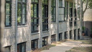 Un bâtiment moderne avec une façade en briques, de grandes fenêtres et un chemin menant à une entrée fermée par un portail.