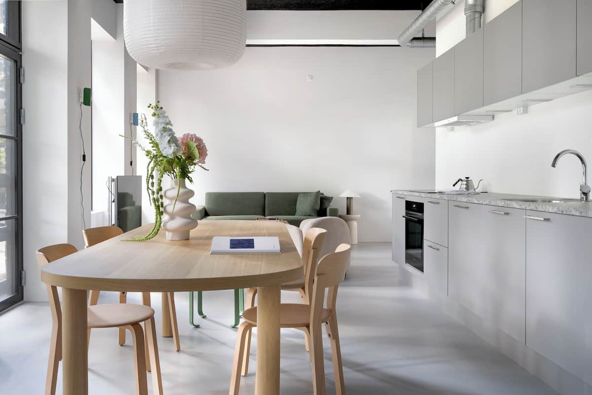 Een moderne keuken met een eethoek, met een houten tafel, stoelen en een vaas met bloemen.