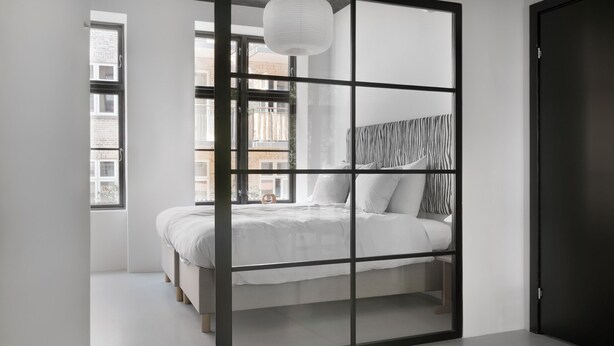 Une chambre moderne avec un grand lit, une vue sur la ville par la fenêtre et une porte sombre.