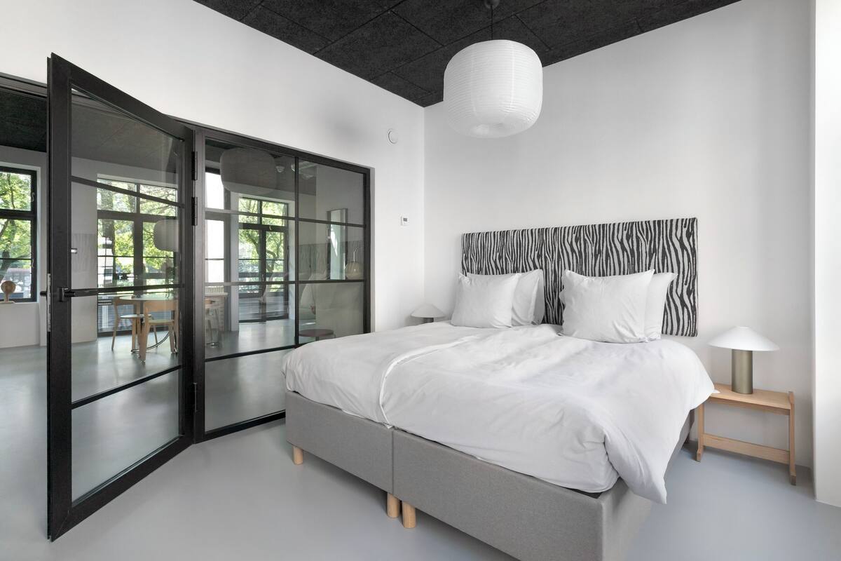 Een moderne slaapkamer met een groot bed, een hoofdbord met zebrapatroon, een glazen deur naar een balkon en een hanglamp.