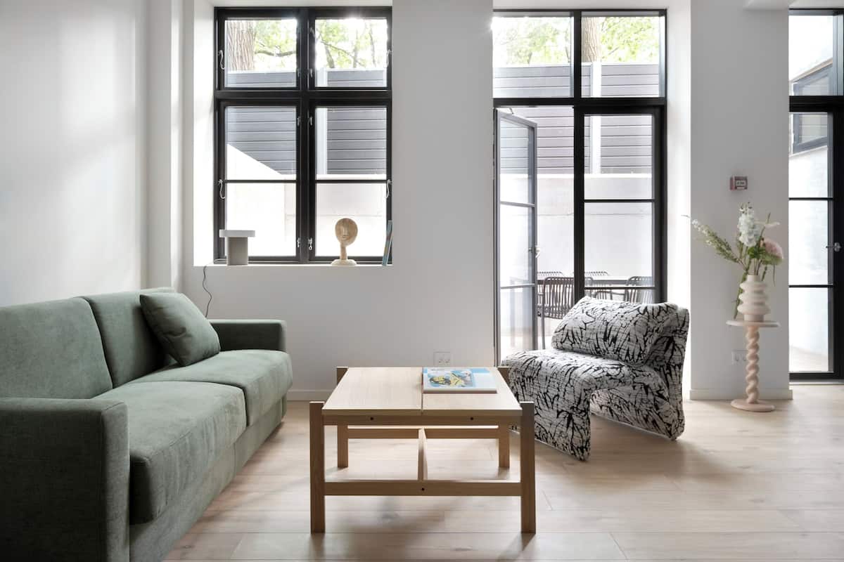 Een moderne woonkamer met een groene bank, een houten salontafel en een fauteuil met een patroon.