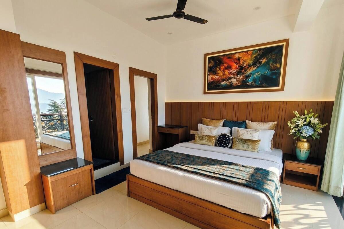 Una camera da letto con un letto grande, una testiera in legno, una ventola a soffitto, un quadro, un comodino, un vaso con fiori e vista attraverso una porta.
