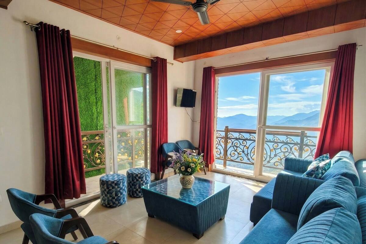 Un'ampia zona giorno con divano, tavolino da caffè e due pouf decorati. Grandi finestre offrono vista sull'esterno.