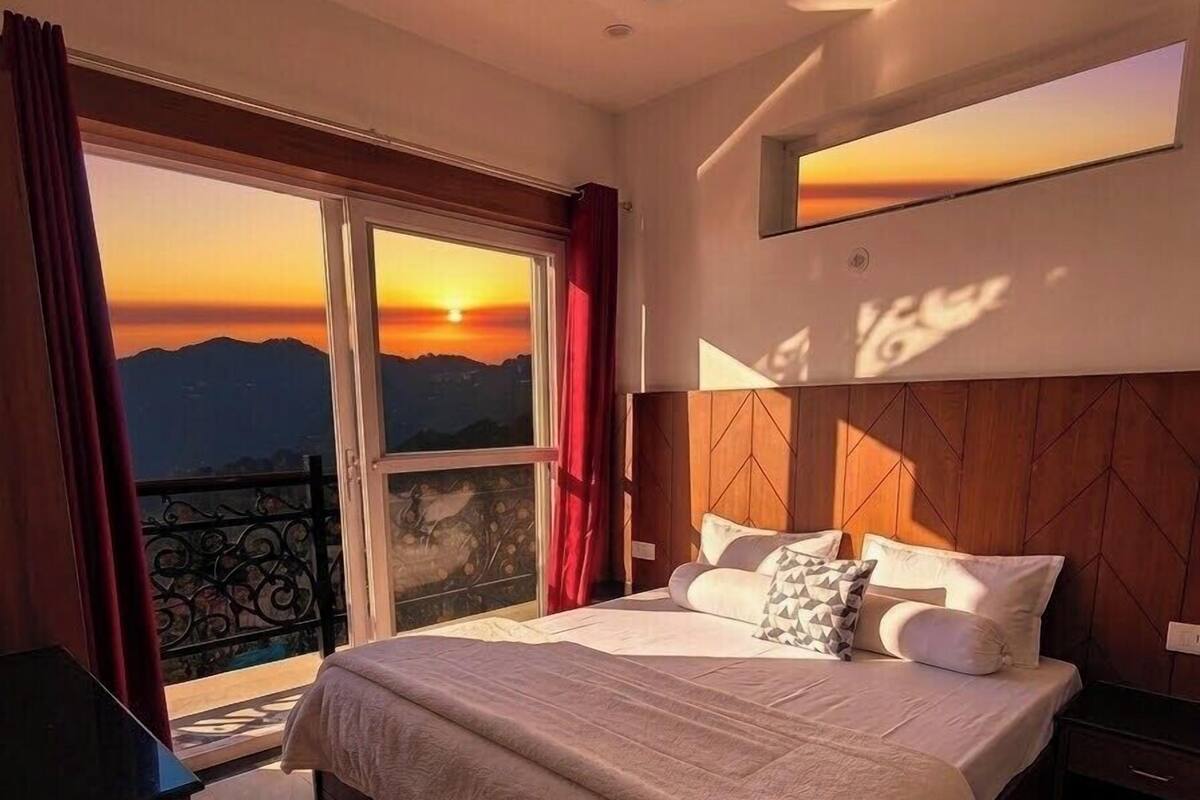 Una camera da letto con un letto, una ventola a soffitto, un comodino, una televisione e vista sul tramonto attraverso una grande finestra.