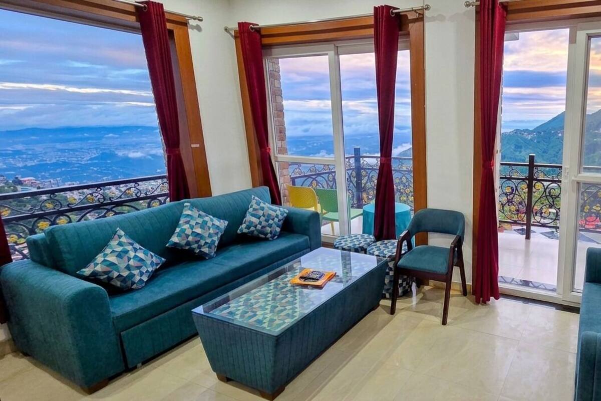 Un soggiorno con due divani, un tavolino da caffè e una poltrona, con un balcone e un televisore fissato alla parete.